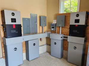 FMS Off Grid Battery Installation Industrial electrical room with four gray 18K PV inverters and service panels on wooden walls.